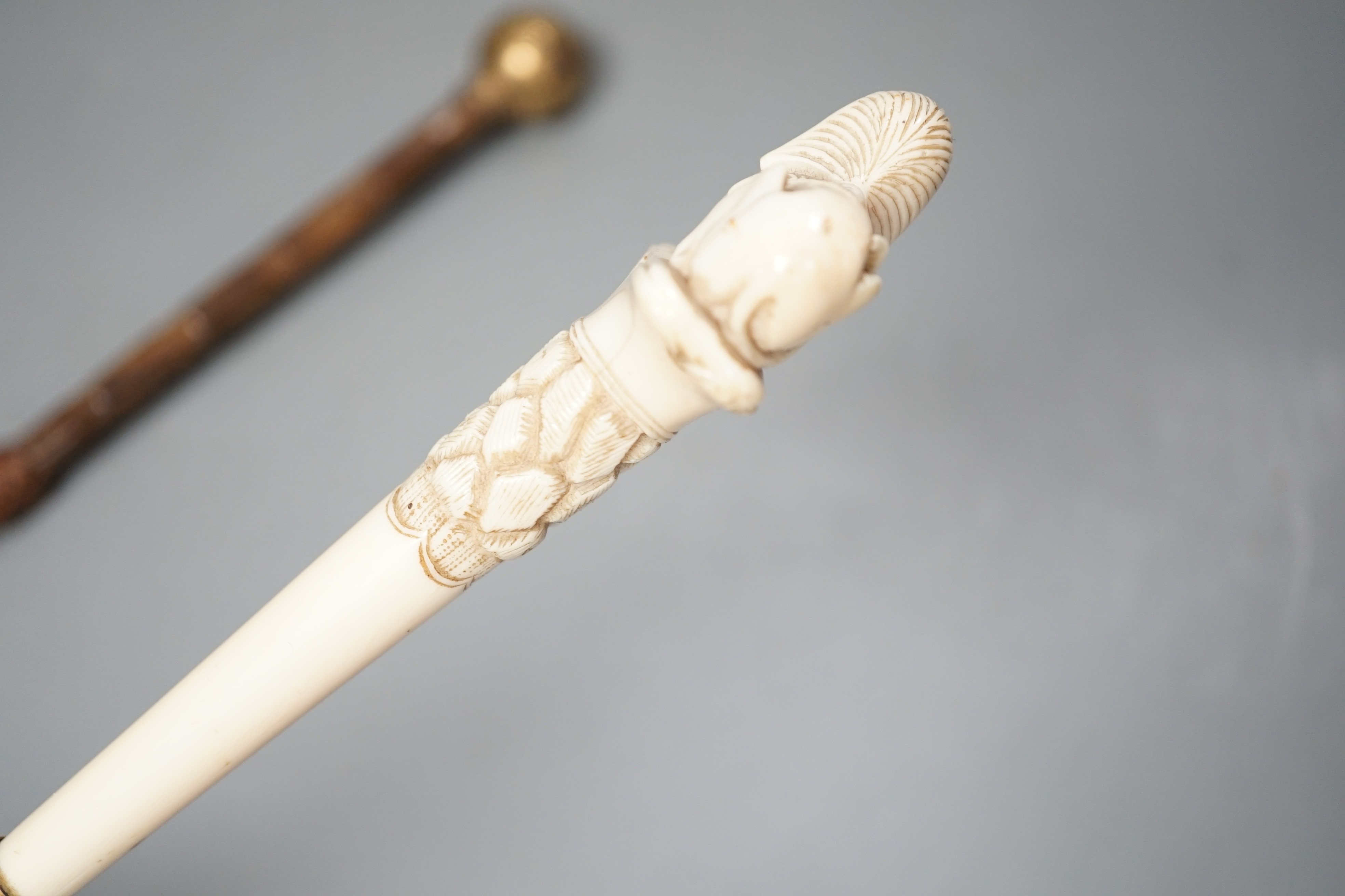 An early 20th century ivory ‘sphinx’ parasol handle, 84cm, together with another gold and iron damascened parasol handle, 62cm